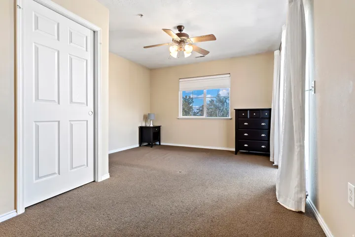 Carpeted room featuring a ceiling fan with integrated lighting, a window with a roller shade, and a paneled closet door