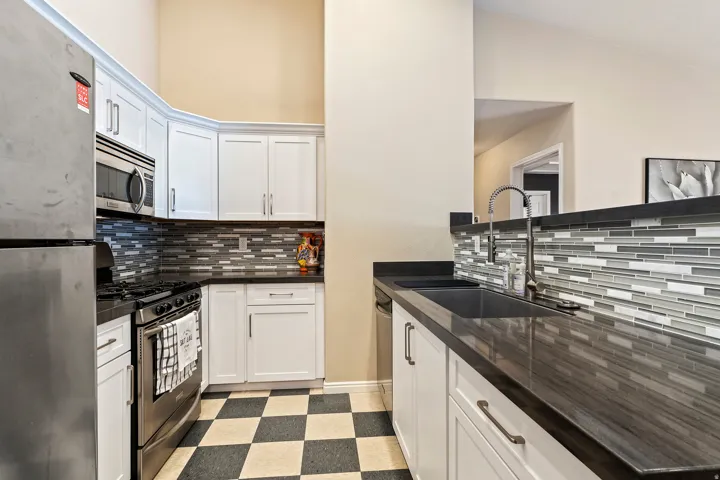 Kitchen featuring white cabinetry, dark countertops, a mosaic tile backsplash, and checkerboard floor tiles