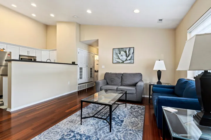 Vaulted ceilings, wood-finish flooring, recessed lighting, and kitchen with white cabinetry and stainless steel appliances