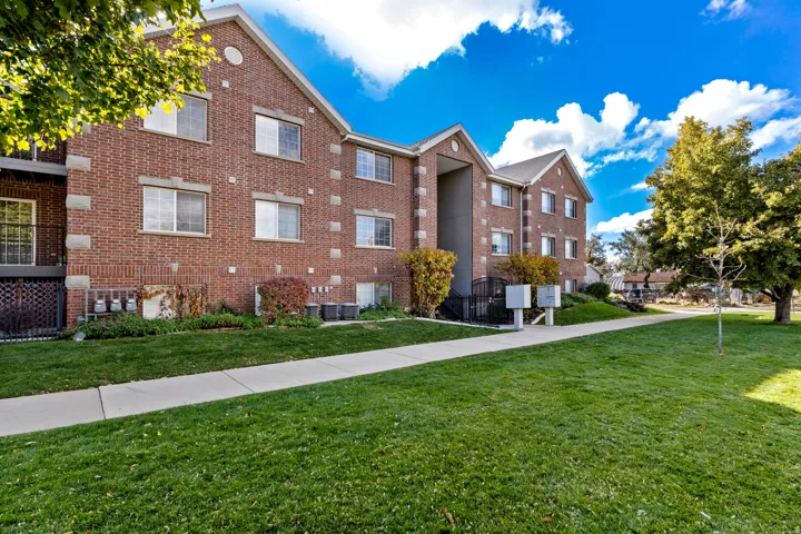 Brick facade apartment building with multiple windows, balconies, and a paved walkway