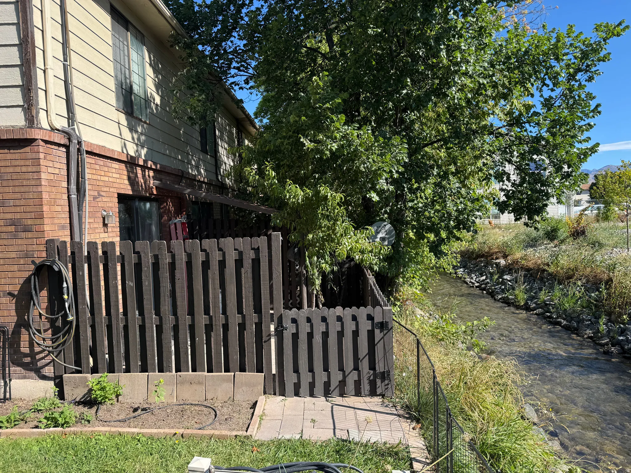 Brick and siding exterior with a patio, bordered by a dark wood fence and a tranquil water feature