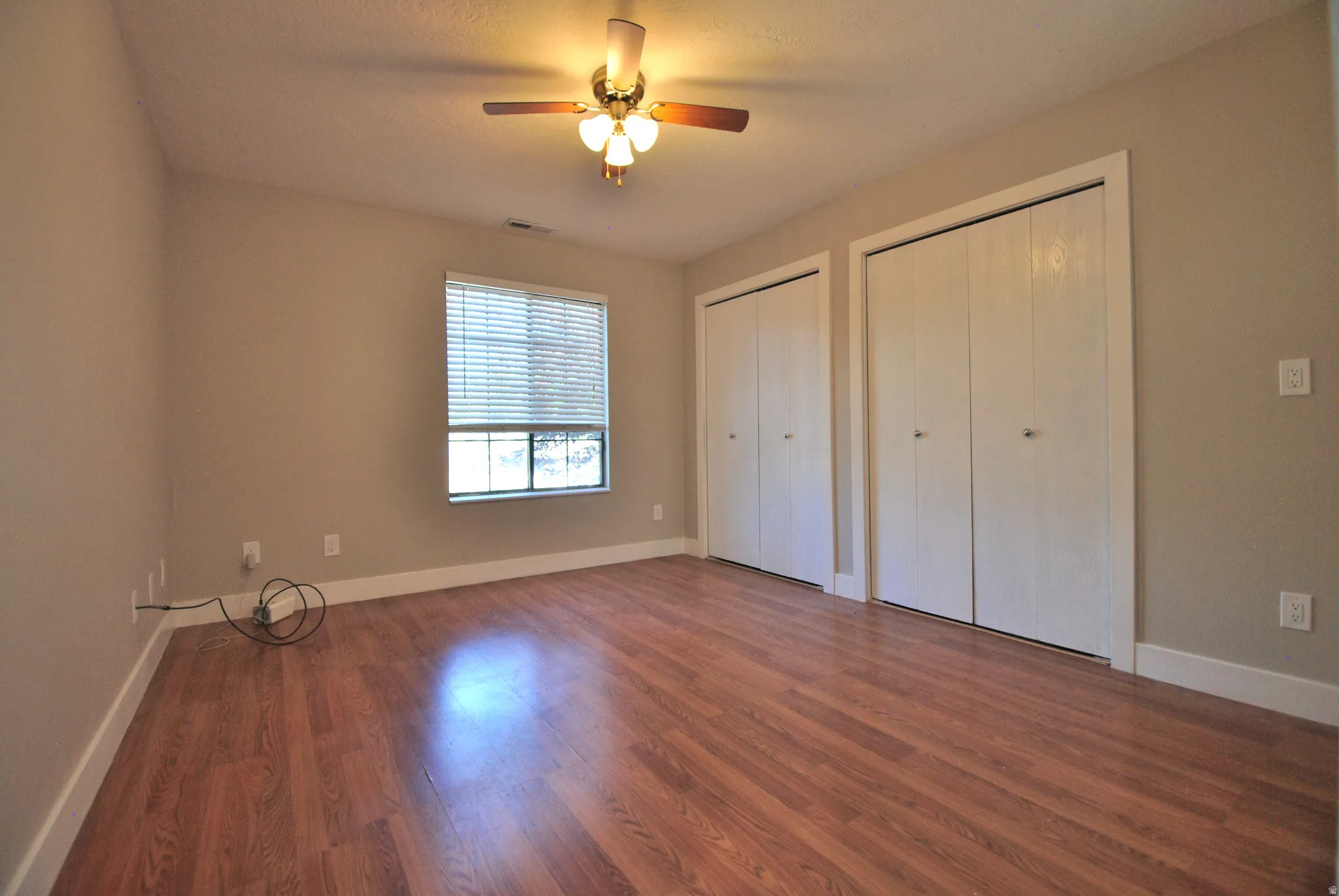 Wood-finish flooring with a neutral wall color, two built-in closets, and a ceiling fan with integrated lighting