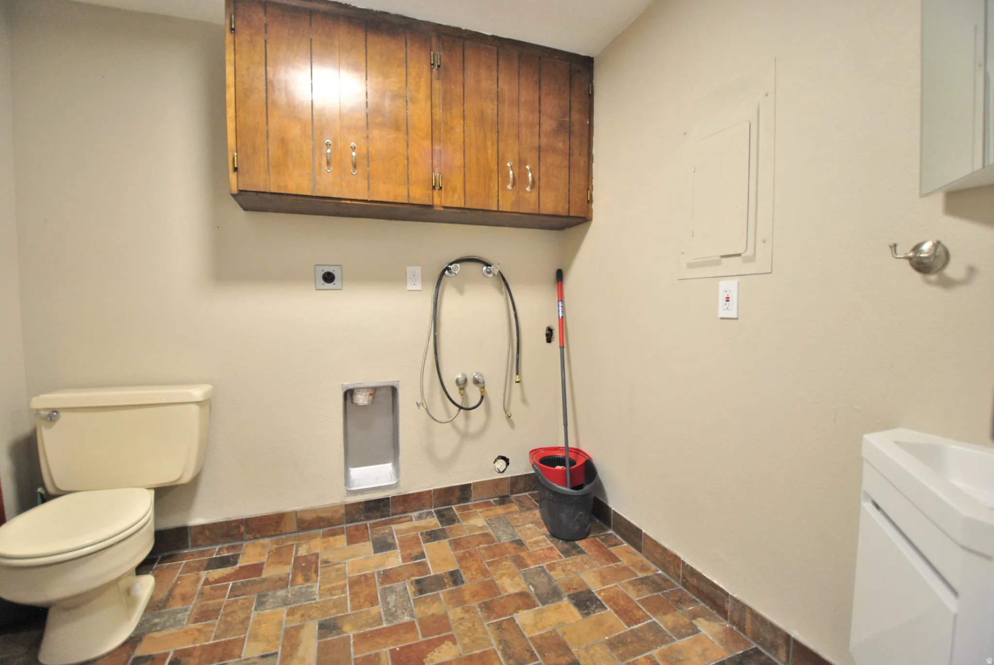 Tile flooring, wall-mounted cabinetry, single toilet, pedestal sink, and laundry hookups