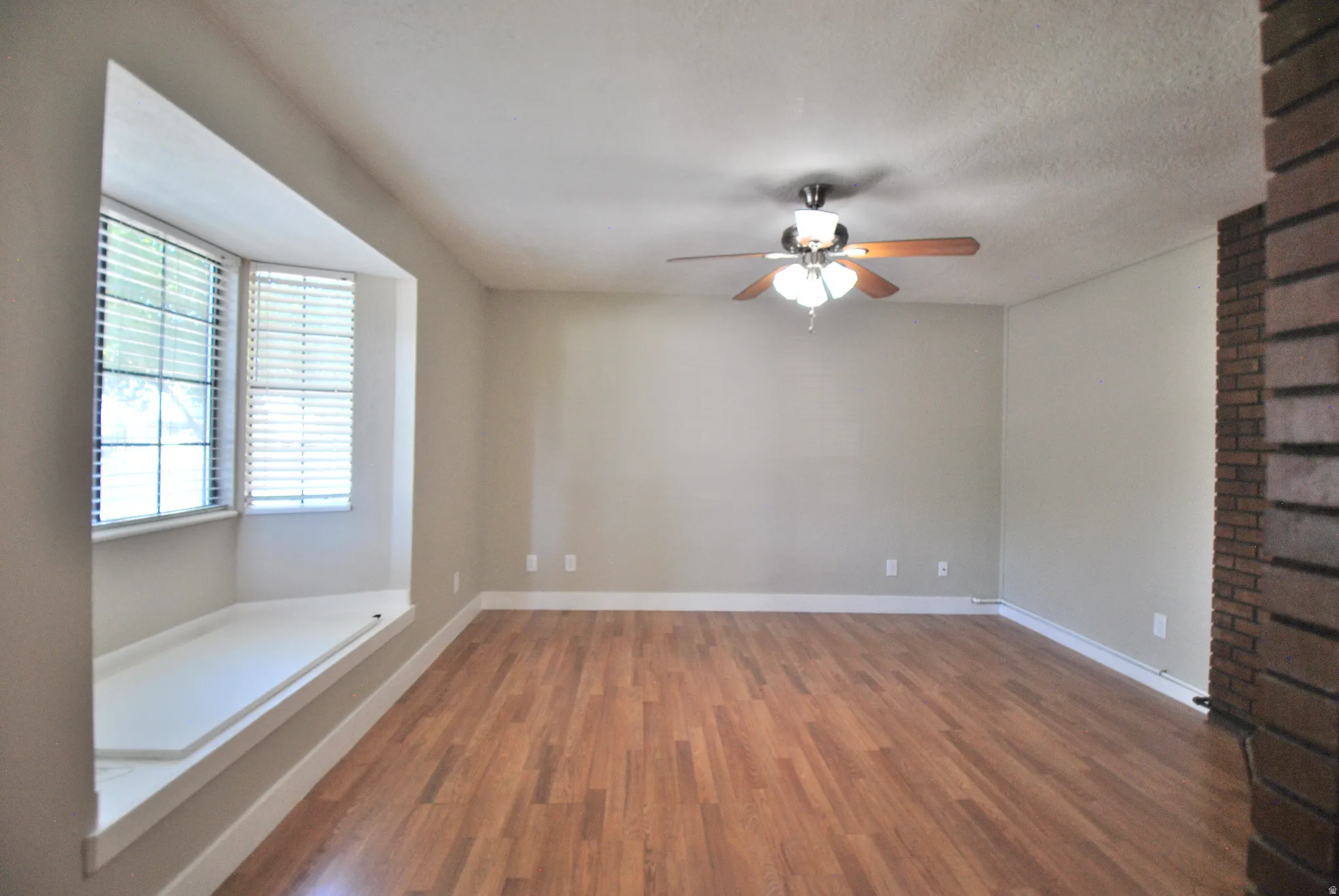 Expansive room featuring wood-finish flooring, a ceiling fan with integrated lighting, and a bay window with a built-in window seat