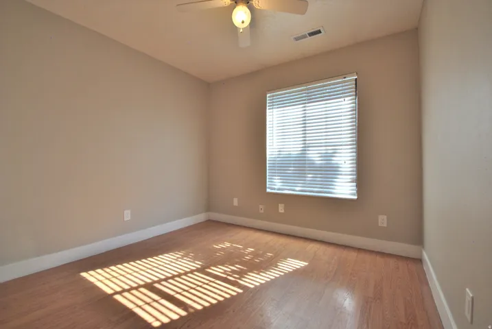 Light-filled room featuring wood-finish flooring, neutral wall tones, window blinds, and a ceiling fan