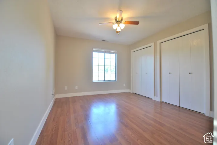 Wood-finish flooring, ceiling fan with integrated lighting, window with grid pattern, and two bi-fold door closets