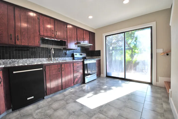 Kitchen featuring wood cabinetry, dark subway tile backsplash, light-toned countertops, and stainless steel appliances