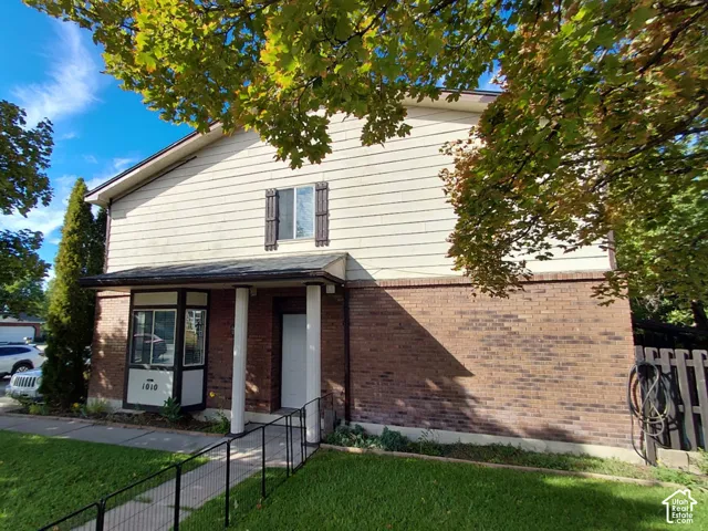 Brick and siding exterior, covered porch entry, bay window with address numbers, upper-level window with decorative shutters, and established landscaping