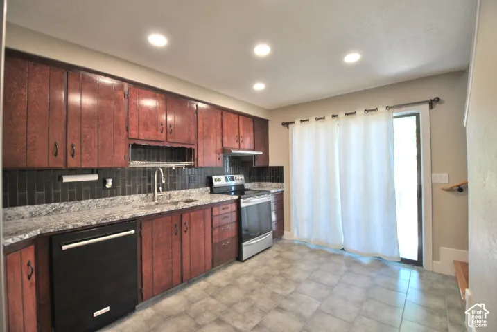 Wood-finish cabinetry, light-toned countertops, dark subway tile backsplash, stainless steel range, and tile flooring