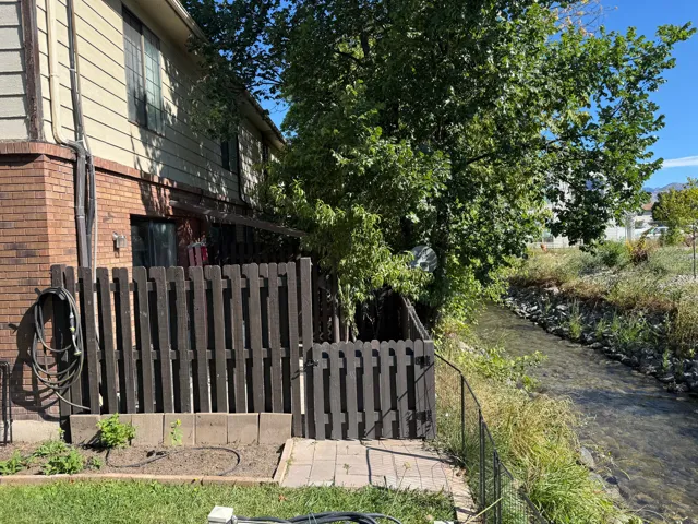 Brick and siding exterior with a patio, bordered by a dark wood fence and a tranquil water feature