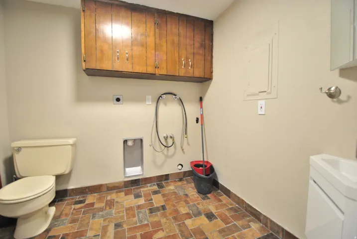 Tile flooring, wall-mounted cabinetry, single toilet, pedestal sink, and laundry hookups