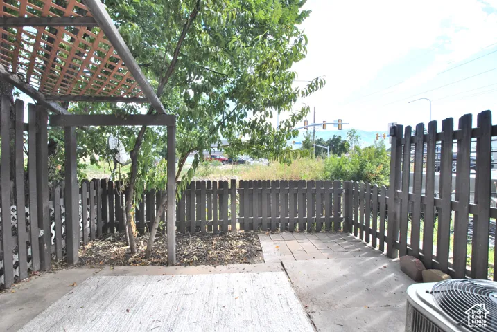 Concrete patio area with a wooden privacy fence, lattice-covered pergola, and mature trees