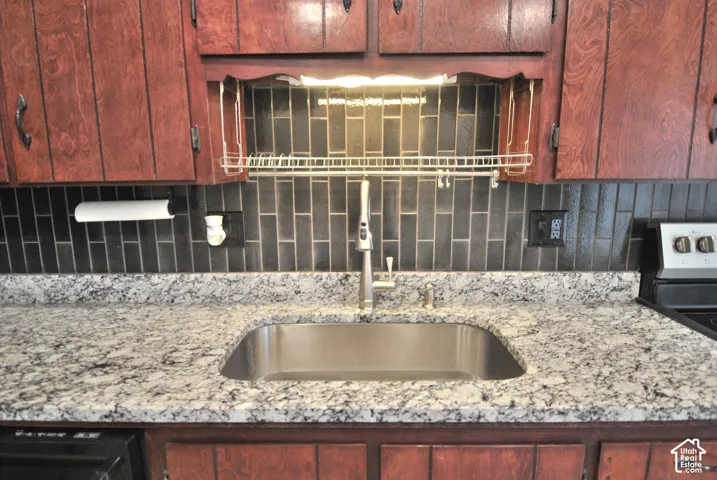 Wood-finish cabinetry paired with a tile backsplash, granite countertops, and a stainless steel sink