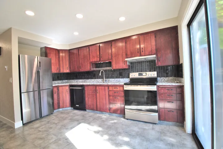 Kitchen featuring wood cabinetry, stainless steel appliances, dark subway tile backsplash, and light-toned tile flooring