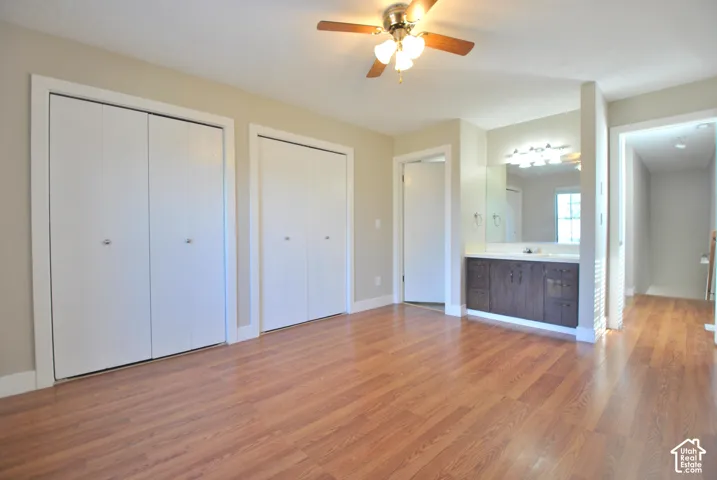 Wood-finish flooring, two bi-fold closet units, ceiling fan with light fixture, vanity with integrated sink, and wall-mounted mirror