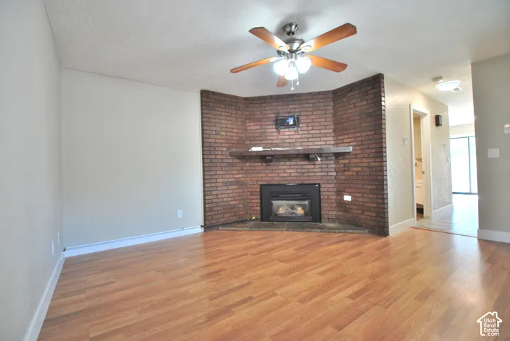 Wood-finish flooring throughout, brick fireplace with a built-in mantel, and a ceiling fan with integrated lighting