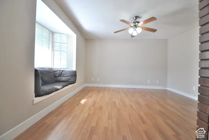 Hardwood-style flooring throughout, bay window with integrated bench seating, and a ceiling fan with integrated lighting