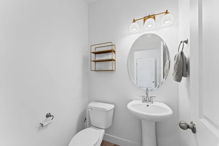 Pedestal sink with chrome faucet, oval wall mirror, three-light vanity fixture with opaque globes, and a two-tier metal wall shelf