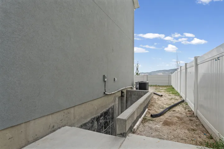 Concrete foundation with stucco exterior, a concrete window well, and a white privacy fence