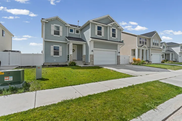 Two-story residence with light blue siding, stone veneer accents, an attached garage, and a covered front entry
