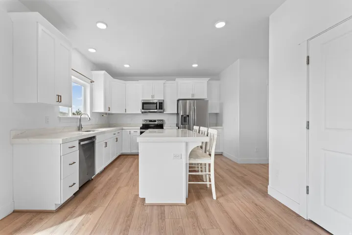 White cabinetry, light-toned wood-finish flooring, recessed lighting, stainless steel appliances, and a central island with counter seating