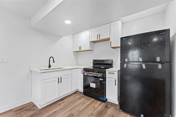 Modern kitchen featuring white cabinetry with brushed metal hardware, wood-finish floating shelves, quartz countertops, a black gas range with blue accent lighting, and a black refrigerator
