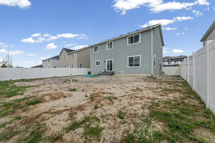 Expansive rear yard with a perimeter vinyl fence, featuring a two-story exterior with multiple windows and a sliding glass door