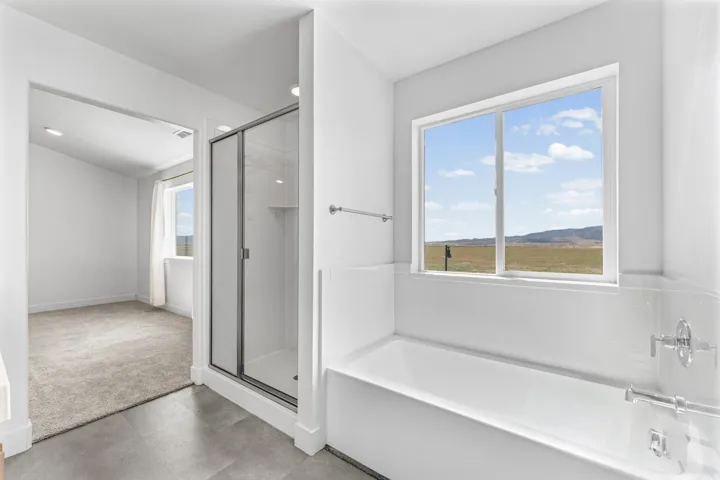 Glass-enclosed shower, white soaking tub, window offering expansive outdoor scenery, polished chrome fixtures, and recessed lighting