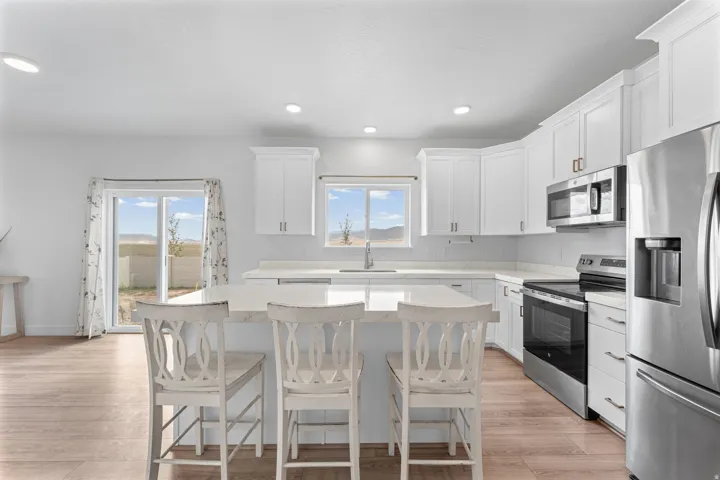 White cabinetry, stainless steel appliances, central island with seating, light wood-finish flooring, and recessed lighting