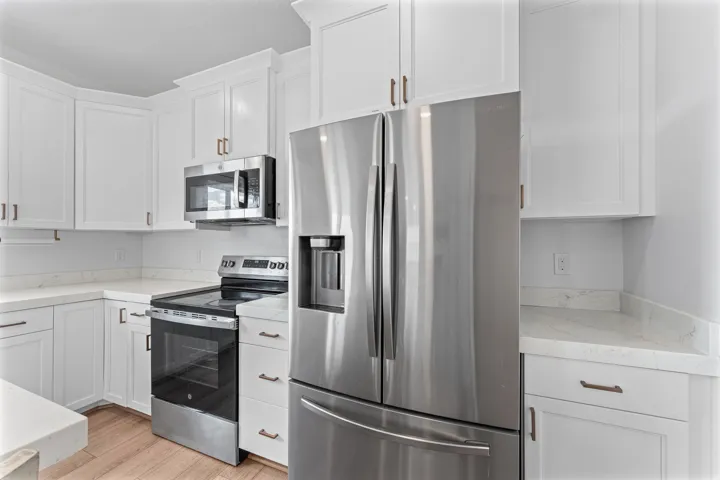 White cabinetry with bronze hardware, stainless steel appliances, light-toned countertops, and wood-finish flooring