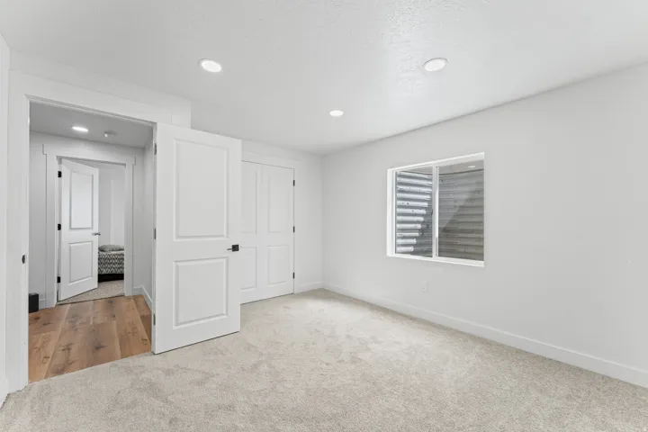 Recessed lighting, light-toned carpeting, white interior doors, and a window with a metal window well