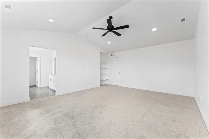 Spacious room featuring vaulted ceilings, recessed lighting, a ceiling fan, plush carpet, and built-in shelving