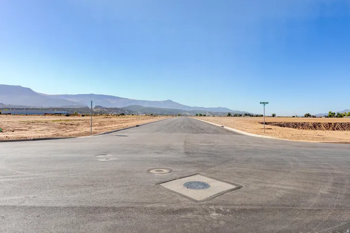 Paved road with curb cuts and utilities in place, surrounded by cleared land and distant mountains