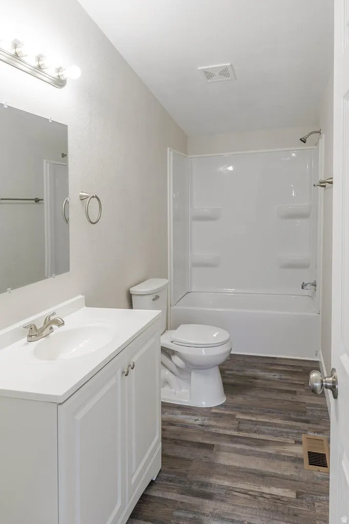 Bathroom featuring a white vanity with integrated sink, brushed nickel faucet, wood-finish flooring, and a white tub/shower combination