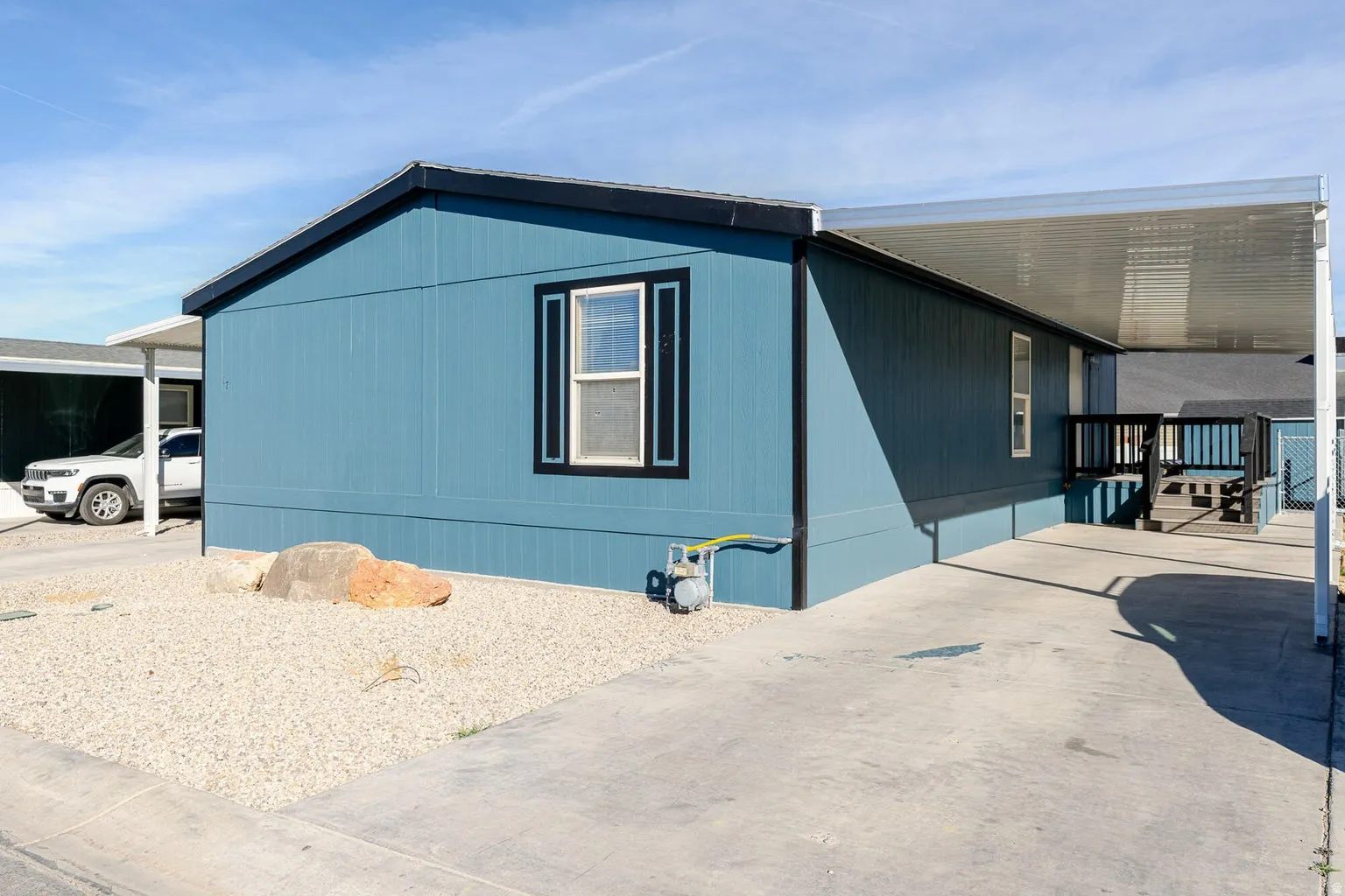 Blue siding exterior with black trim, concrete driveway, gravel landscaping, and a side deck with covered patio