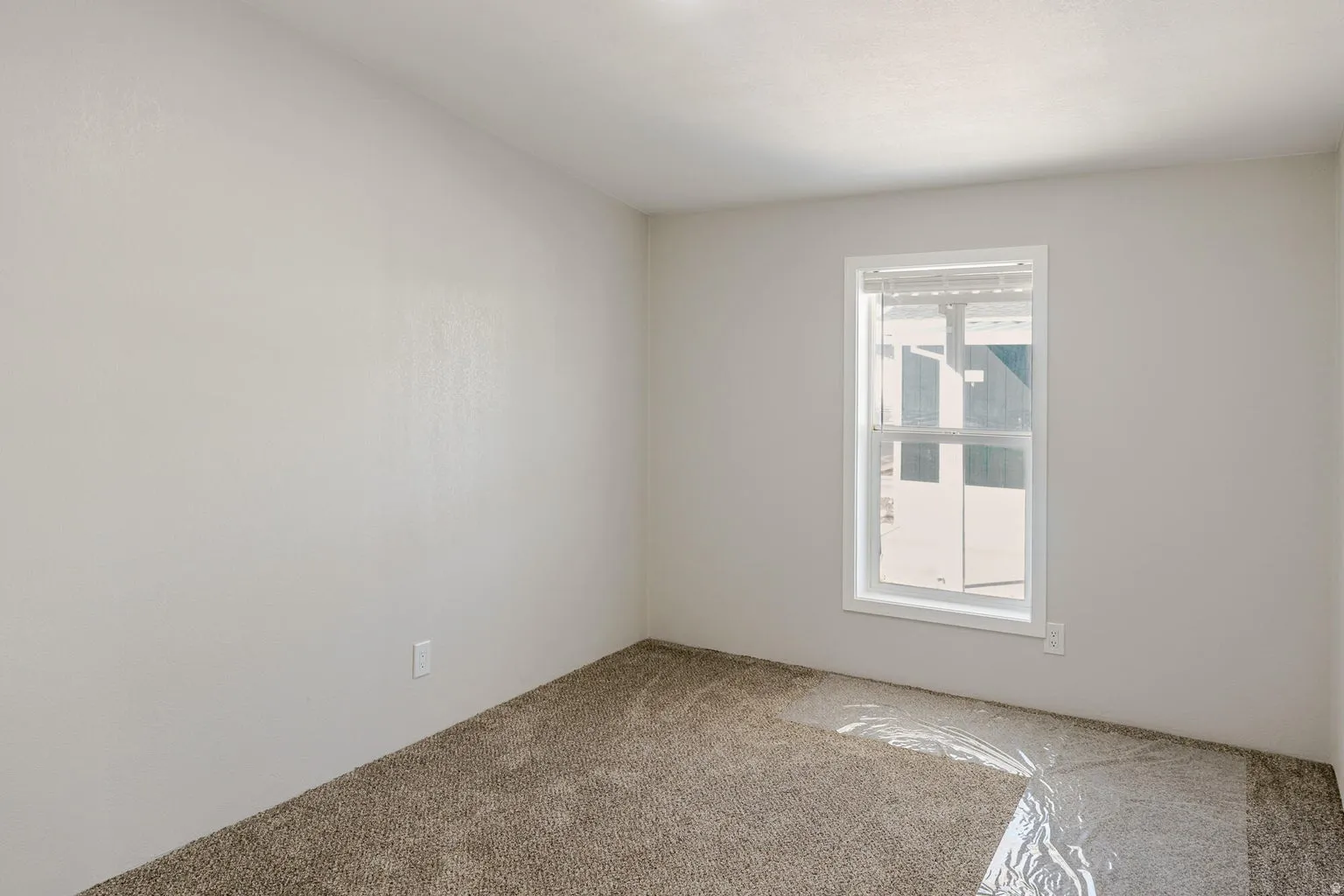 Neutral tone wall finish with a single window and carpeting
