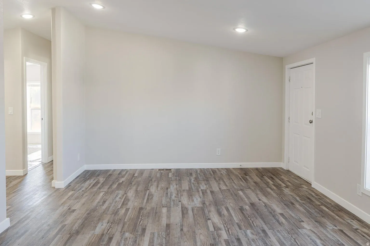 Spacious room featuring wood-finish flooring, recessed lighting, and a paneled entry door