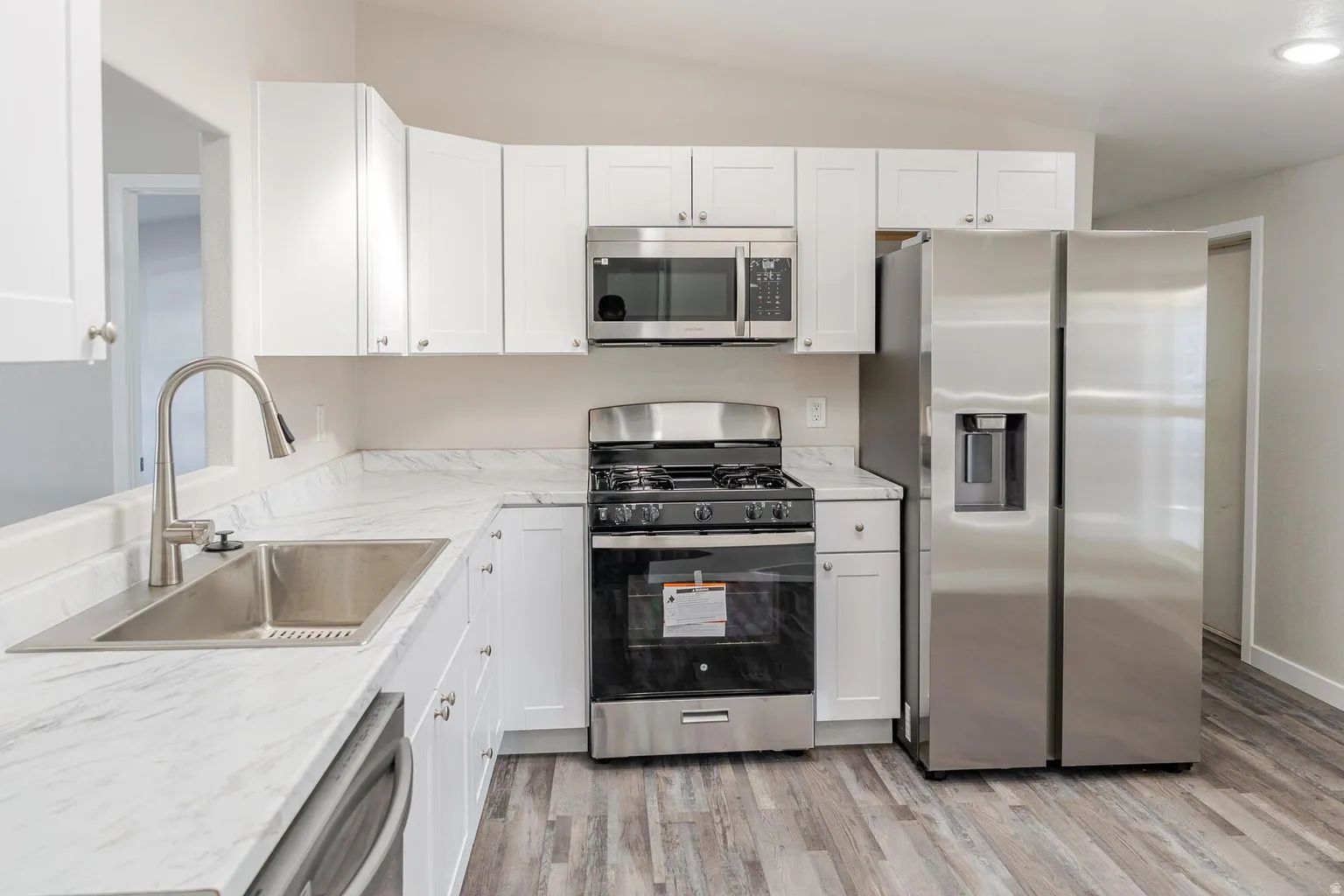 Kitchen featuring white cabinetry, stainless steel appliances, wood-finish flooring, and light-toned countertops