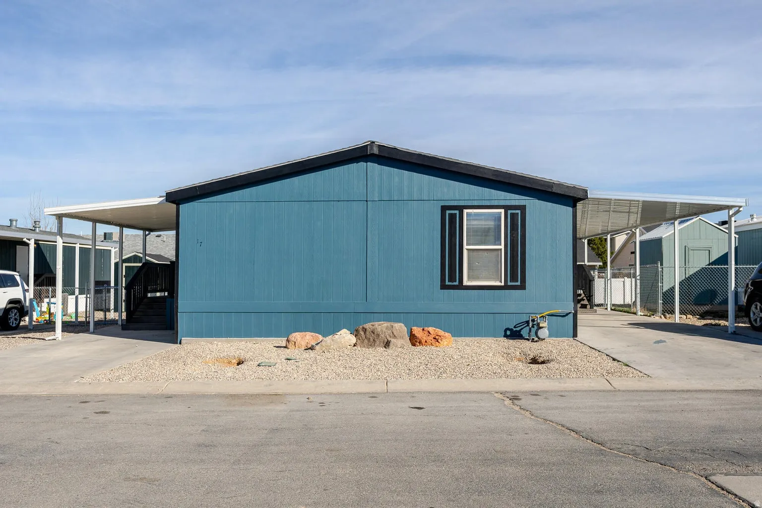 Blue siding exterior with black trim window, gravel landscaping, and dual carport structures