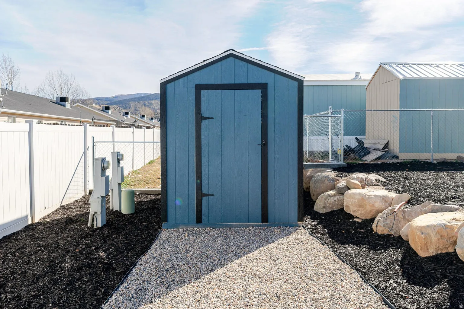 Blue-painted shed with dark trim, gravel path, and rock landscaping