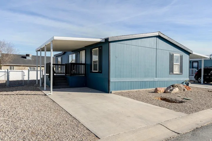 Blue exterior siding, covered carport, concrete driveway, gravel landscaping, and a fenced yard