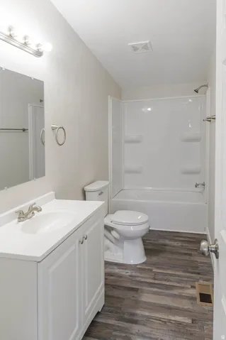 Bathroom featuring a white vanity with integrated sink, brushed nickel faucet, wood-finish flooring, and a white tub/shower combination