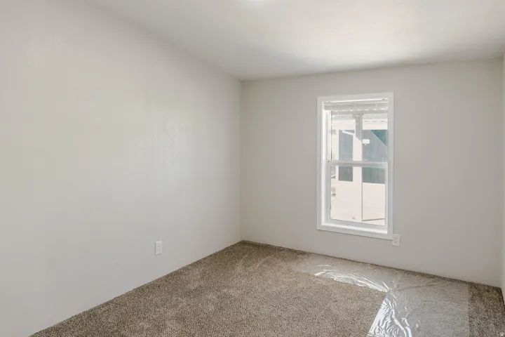 Neutral tone wall finish with a single window and carpeting