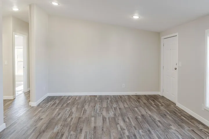 Spacious room featuring wood-finish flooring, recessed lighting, and a paneled entry door
