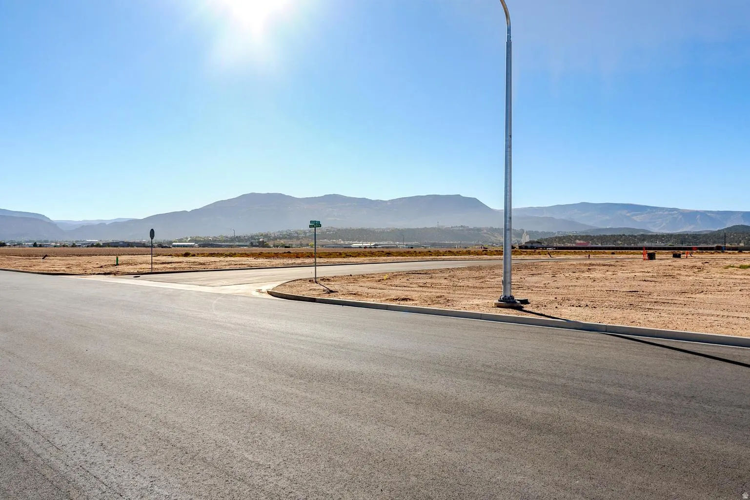Paved road infrastructure with curb and street lighting, surrounded by developable land, with distant mountain scenery