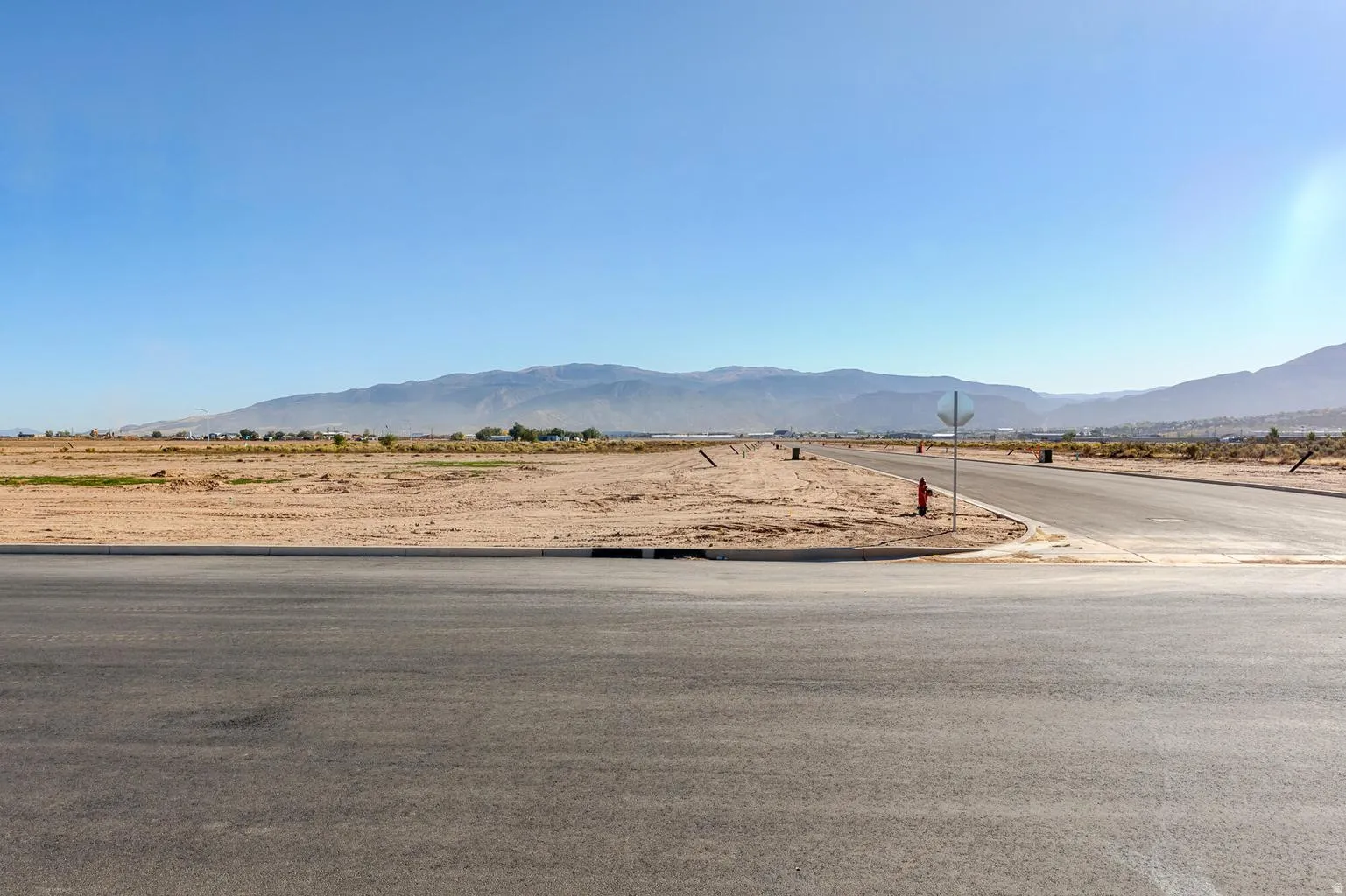 Expansive undeveloped land with a paved street, curb, and visible fire hydrant