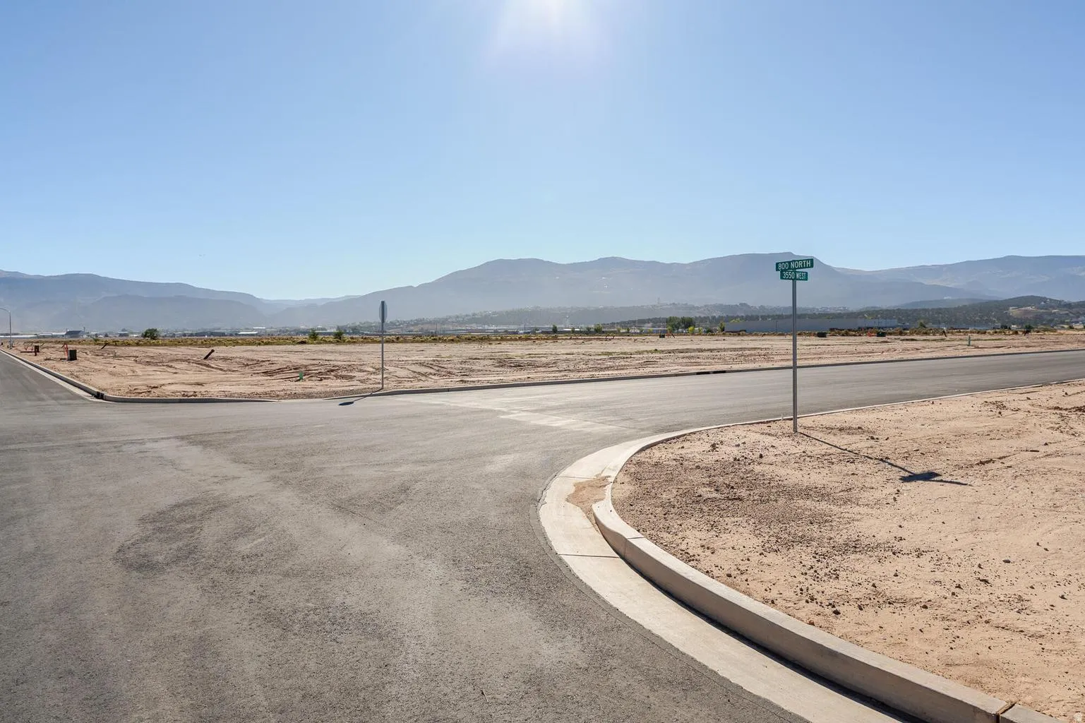 Paved roads, concrete curbing, expansive undeveloped land, and distant mountains
