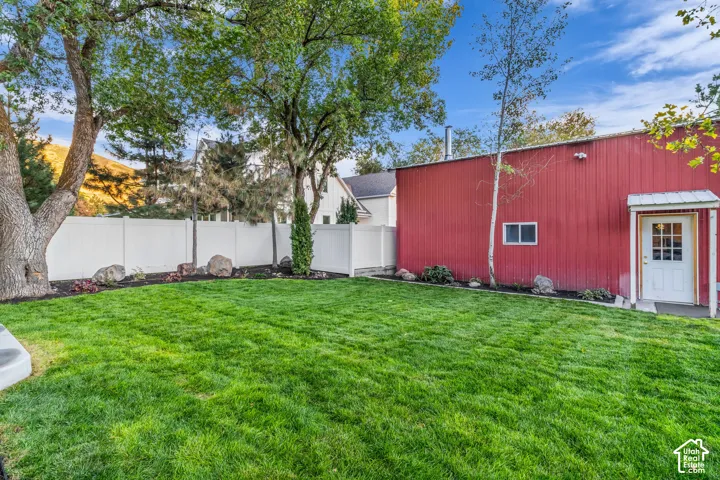 Expansive green lawn, mature trees, white privacy fencing, red metal siding, and a white entry door with an overhang