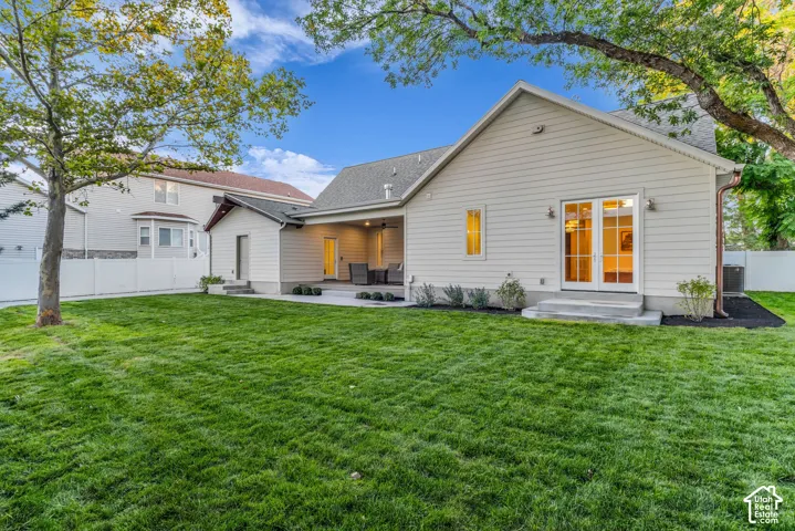 Expansive backyard with a manicured lawn, covered patio, French doors, multiple exterior light fixtures, and a white privacy fence