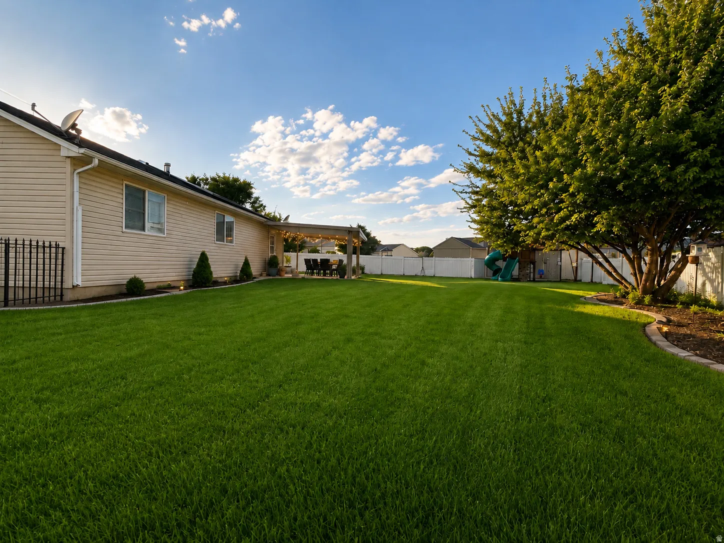 Expansive backyard featuring a manicured lawn, established landscaping, and awning